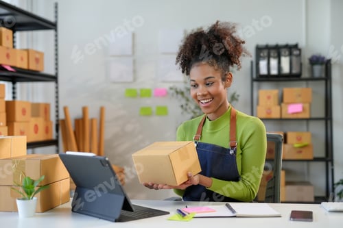 Preview: Smiling young woman working in warehouse, checking online order on tablet and holding package