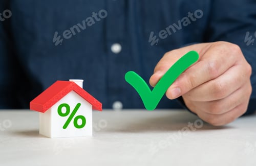 Preview: A man holds a check mark near his house. Mortgage approval at a favorable interest rate.