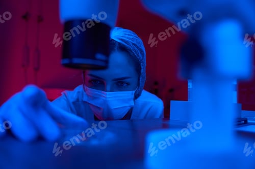 Preview: Cute female places petri mug with biomaterial under powerful microscope