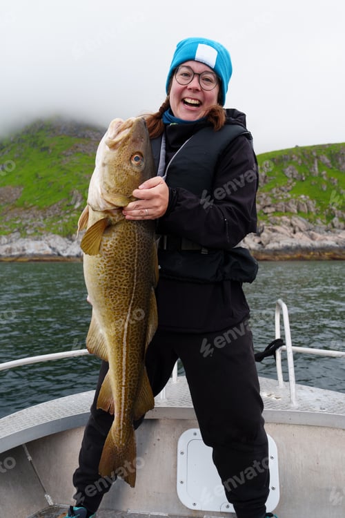 Preview: Happy young woman holding big arctic cod. Norway happy fishing. Fisherwoman with cod fish in hands