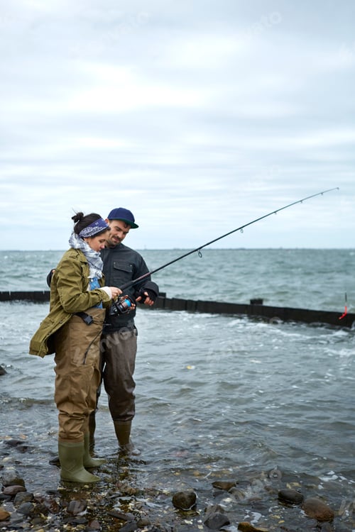 Preview: Young man ankle deep in water teaching girlfriend sea fishing