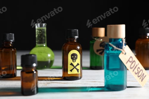 Preview: Bottles of poisons with warning sign on wooden table against black background, closeup