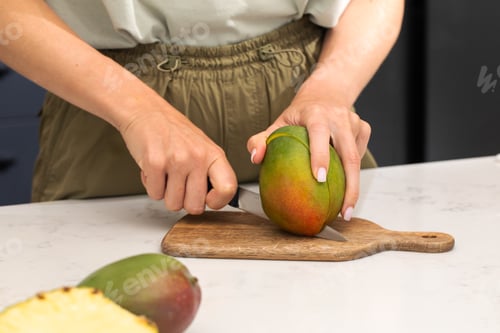 Preview: Person cutting ripe mango on wooden board for fresh summer snack preparation