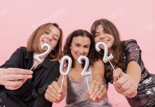 Visualização: Um grupo de garotas está segurando velas dos números 2022 em um fundo rosa.