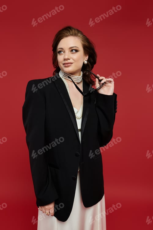 Preview: Elegant young woman exudes confidence in chic attire against a striking red backdrop