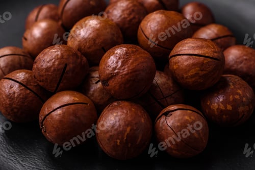 Preview: Delicious roasted macadamia nuts in shell on a dark textured background