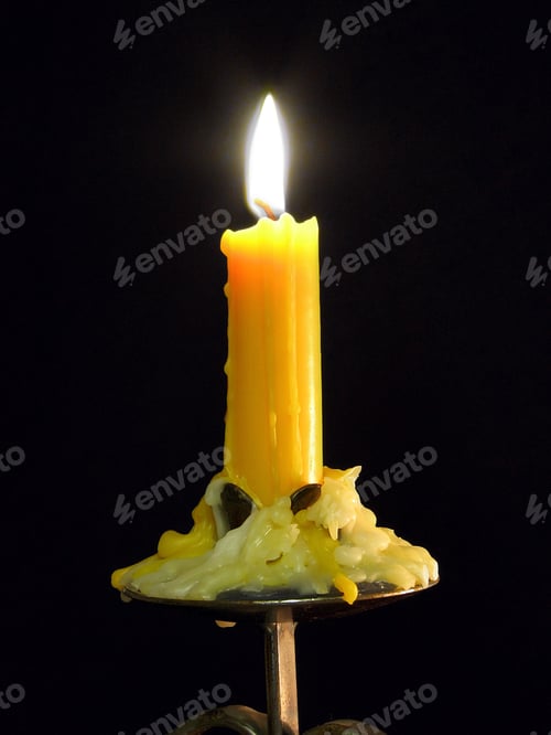 Preview: Partly melted candle burning on a black background