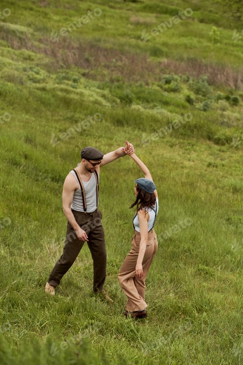 Preview: Smiling bearded man in sunglasses and suspenders having fun with brunette girlfriend in newsboy cap