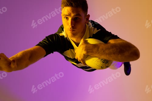Preview: Caucasian male rugby player jumping with rugby ball over pink lighting