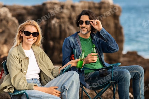 Preview: Friends enjoy refreshing drinks while relaxing on rocks by the sea