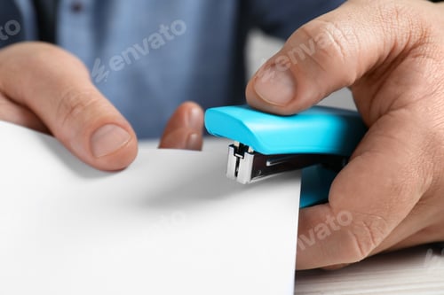 Preview: Man with papers using stapler at white table, closeup