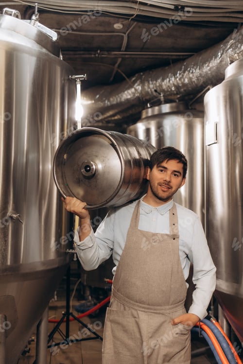 Preview: Portrait of male brewer carrying metal container at brewery factory. Young man holding