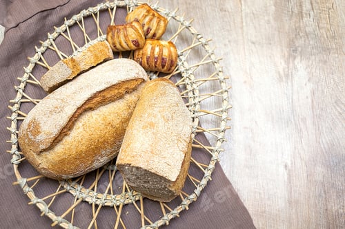 Preview: homemade baked crisp bread sweet buns and baguette on table in basket, baked pastry food. top view.