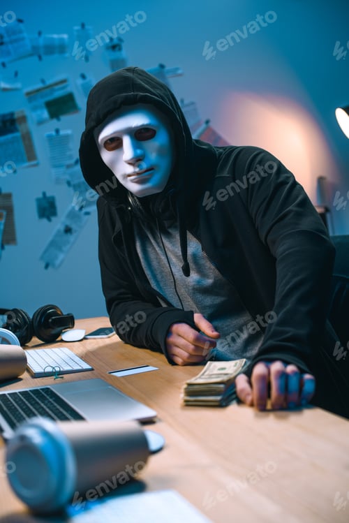 Preview: hacker in mask with stack of money on desk