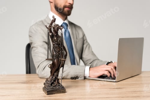 Preview: partial view of lawyer using laptop near themis statue isolated on grey