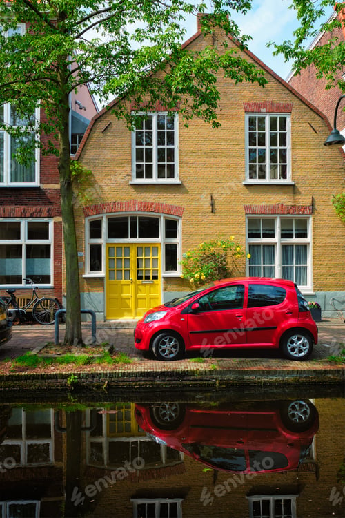 Preview: Red car on canal embankment in street of Delft. Delft, Netherlands