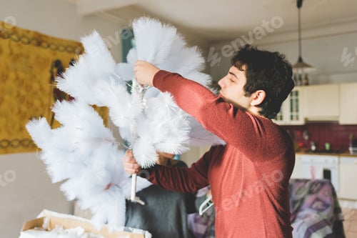 Preview: Young man at home decorating xmas tree