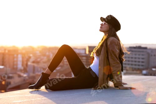 Preview: Woman in Hat Relaxes on City Rooftop at Sunset