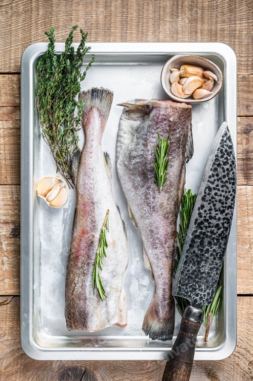 Preview: Raw cod whole fish in steel kitchen tray with thyme and rosemary. Wooden background. Top view