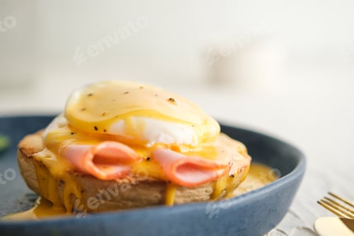 Preview: egg Benedict with hollandaise sauce on blue plate on table in white kitchen