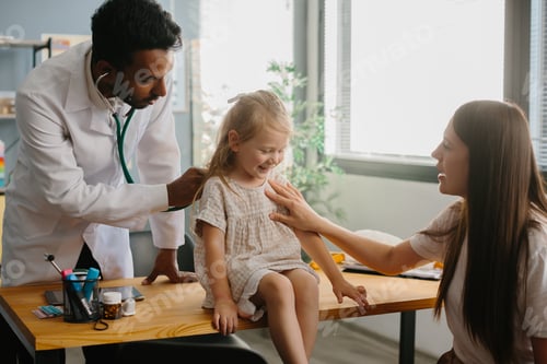 Preview: Smiling pediatrician with stethoscope checking little girl's lungs.