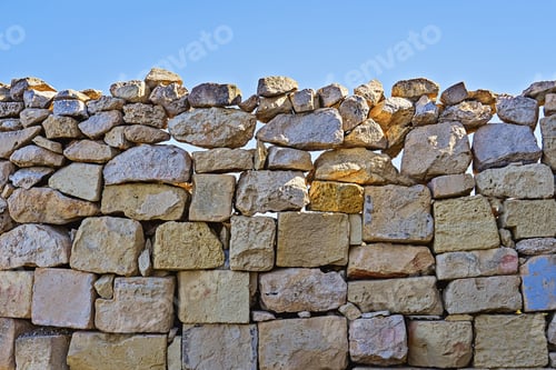 Visualização: Parede de pedra calcária de alvenaria com pedras rachadas contra o céu azul. Textura de construção natural