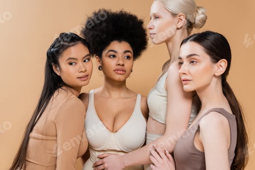 Preview: sensual multicultural women in underwear touching each other while posing isolated on beige