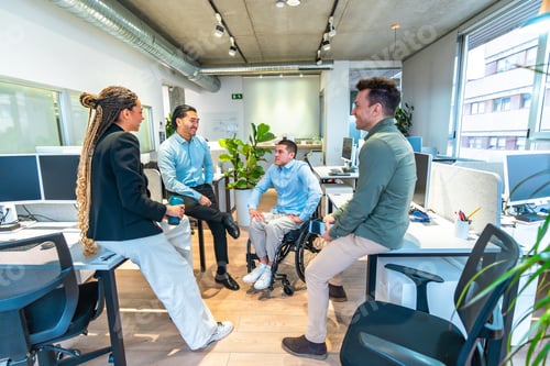 Preview: Diverse business team discussing in modern office with disabled colleague in wheelchair