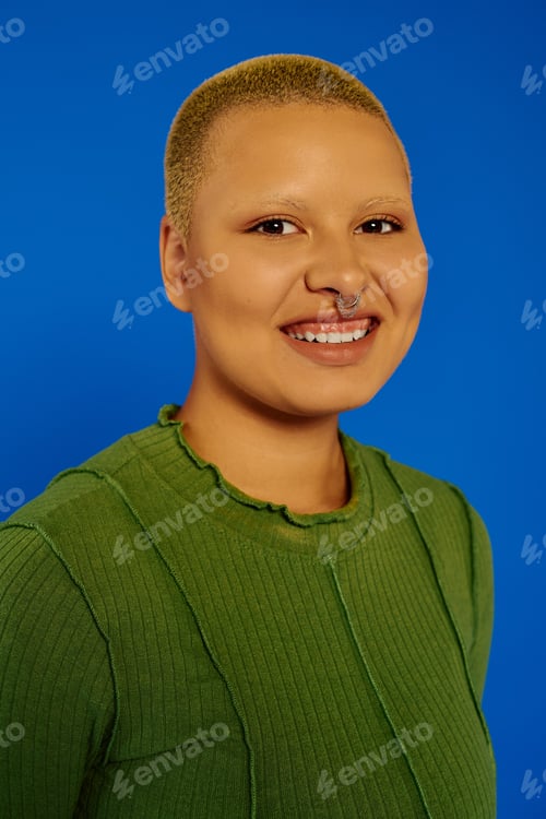 Preview: Stylish young woman smiling brightly against a vibrant blue background in a modern setting