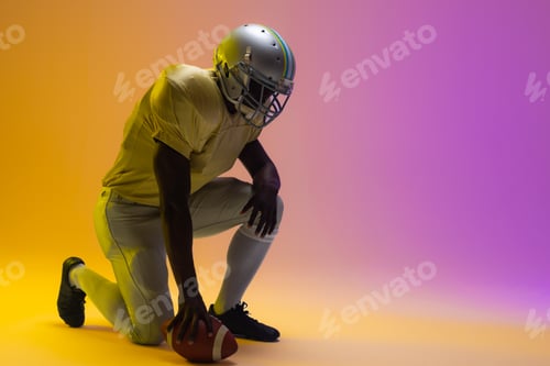 Preview: African american male american football player holding ball with neon yellow and purple lighting