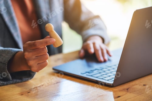 Aperçu: Femme d'affaires dirigeante tenant et choisissant des personnes en bois tout en travaillant sur un ordinateur portable au bureau