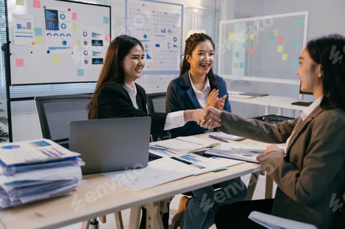 Preview: Group of asian businesswomen shaking hands over a desk in a modern office, celebrating a successful