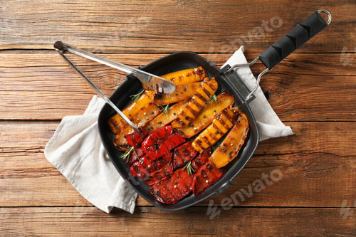 Preview: Delicious grilled peppers with spices in pan and tongs on wooden table, top view