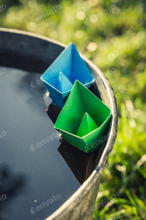 Preview: Handmade paper boats quietly floating on water in garden