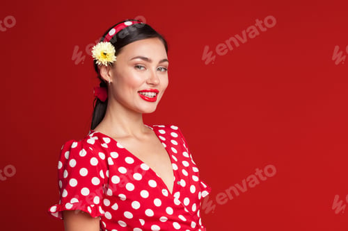 Preview: Woman in red polka dot dress smiles against bright red background in a playful pose