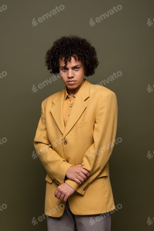 Preview: brunette african american man in trendy yellow blazer looking at camera on olive grey background