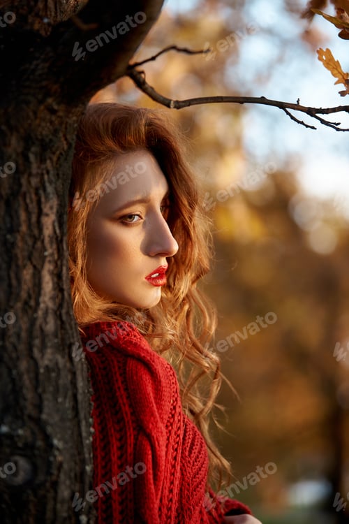 Preview: Redhead young woman in a red sweater walks in the park. Autumn beauty portrait of a fashionable