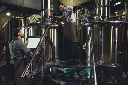 Preview: Male brewers in aprons working with tanks and industrial equipment at the brewery