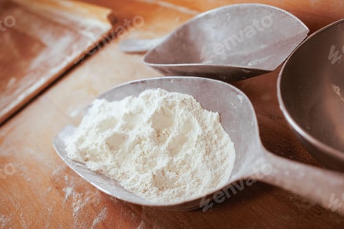 Preview: Closeup of a spoons filled with white flour, resting on a rustic wooden