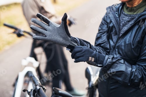 Preview: A midsection of active senior couple standing outdoors with electobikes, putting on gloves.