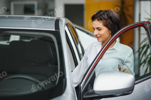 Preview: Finally new car! Young female customer checking out a new car at the car dealership