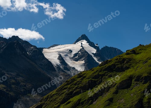 Preview: Low angle of a snowy mountain top with grass in Glacier national park and a blue sky background