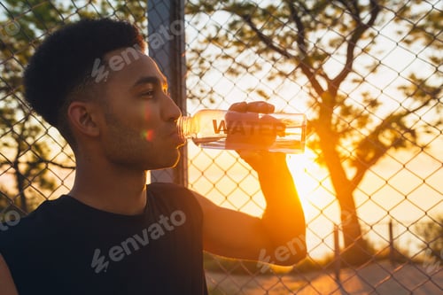 Preview: black man doing sports in morning, drinking water on basketball court on sunrise
