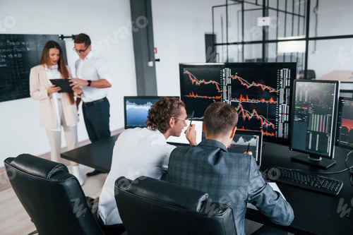 Preview: Attention to details. Team of stockbrokers works in modern office with many display screens