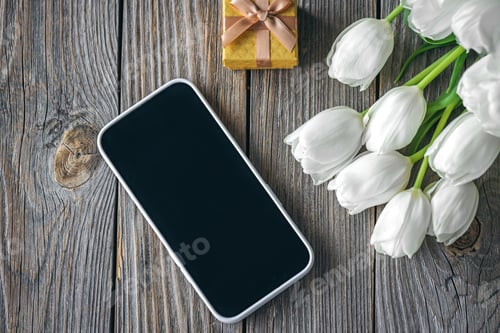 Preview: Smartphone, gift box and bouquet of flowers on a wooden background, top view.
