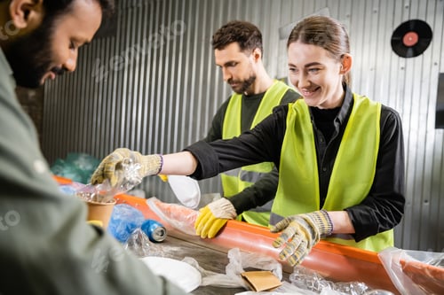 Preview: Positive worker in protective gloves and reflective vest taking plastic trash from conveyor