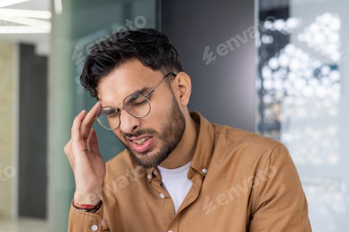 Preview: Man experiencing headache in office, feeling pain and stress