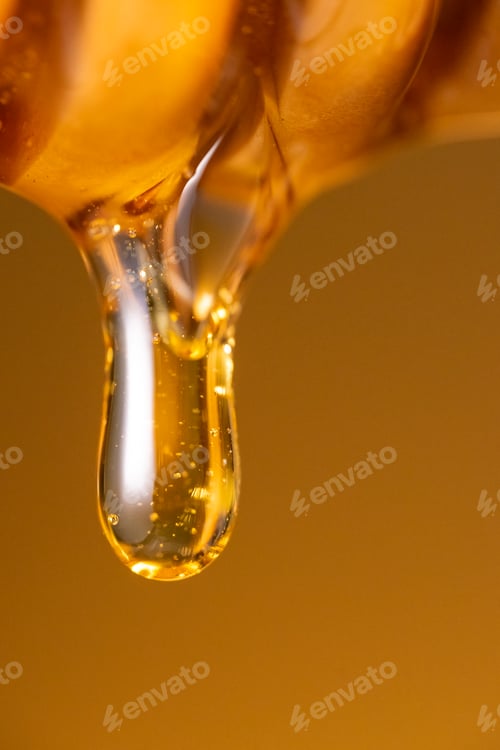 Preview: Honey dripping from dipper wooden honey stick macro shot over dark yellow background