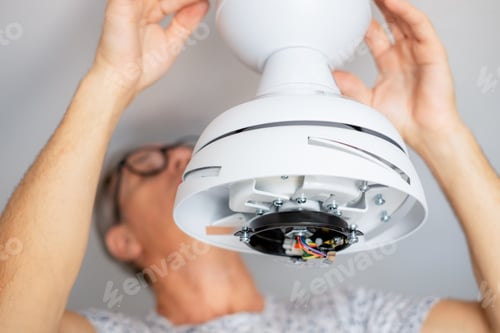 Preview: Close up on electrician man 's hands installing a paddle fan on the ceiling of home living room