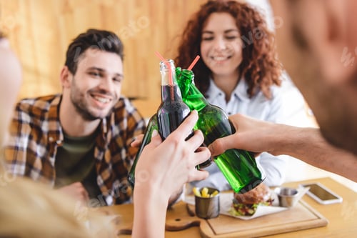 Preview: selective focus of glass bottles with beverage holding by friends